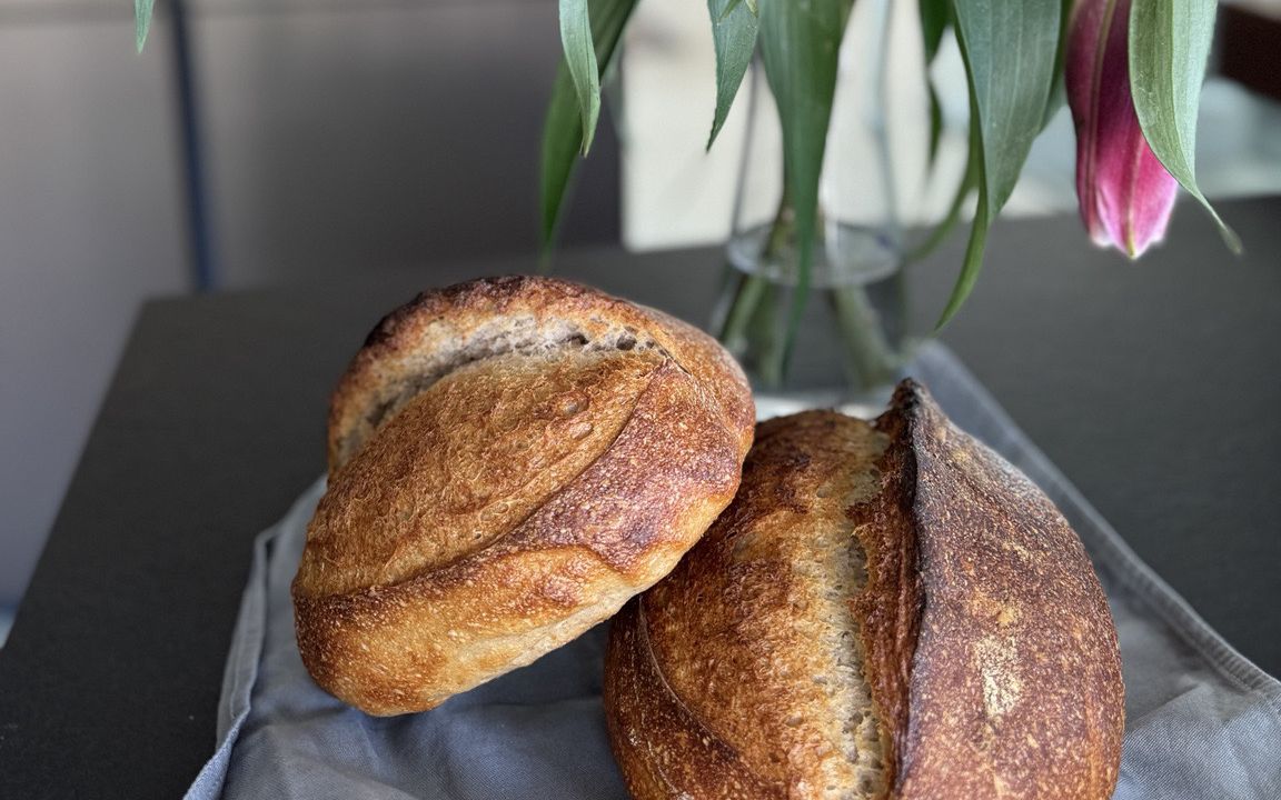 Zwei kleine Krustenbrote vor einem Lilienstrauß